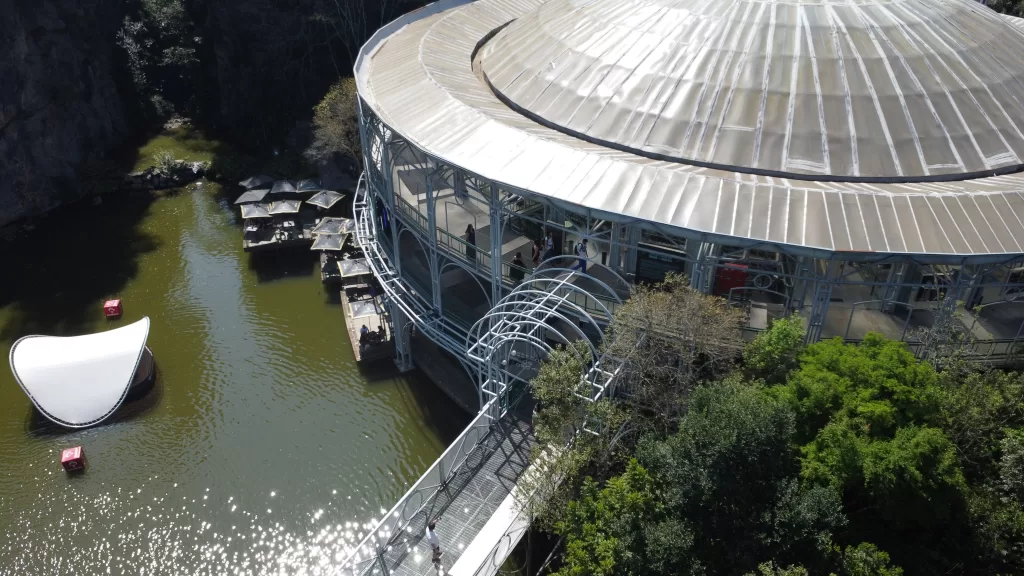 Aerial view of Opera de Arame in Curitiba, showing a local nature, outdoor seating, and a little music venue in the middle of the lake.