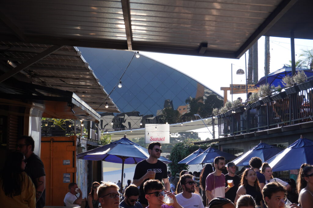 Sunset eatery filled with dozens of visitors. Behind the many shops and visitors, Oscar Niemeyer's eye museum can be seen.