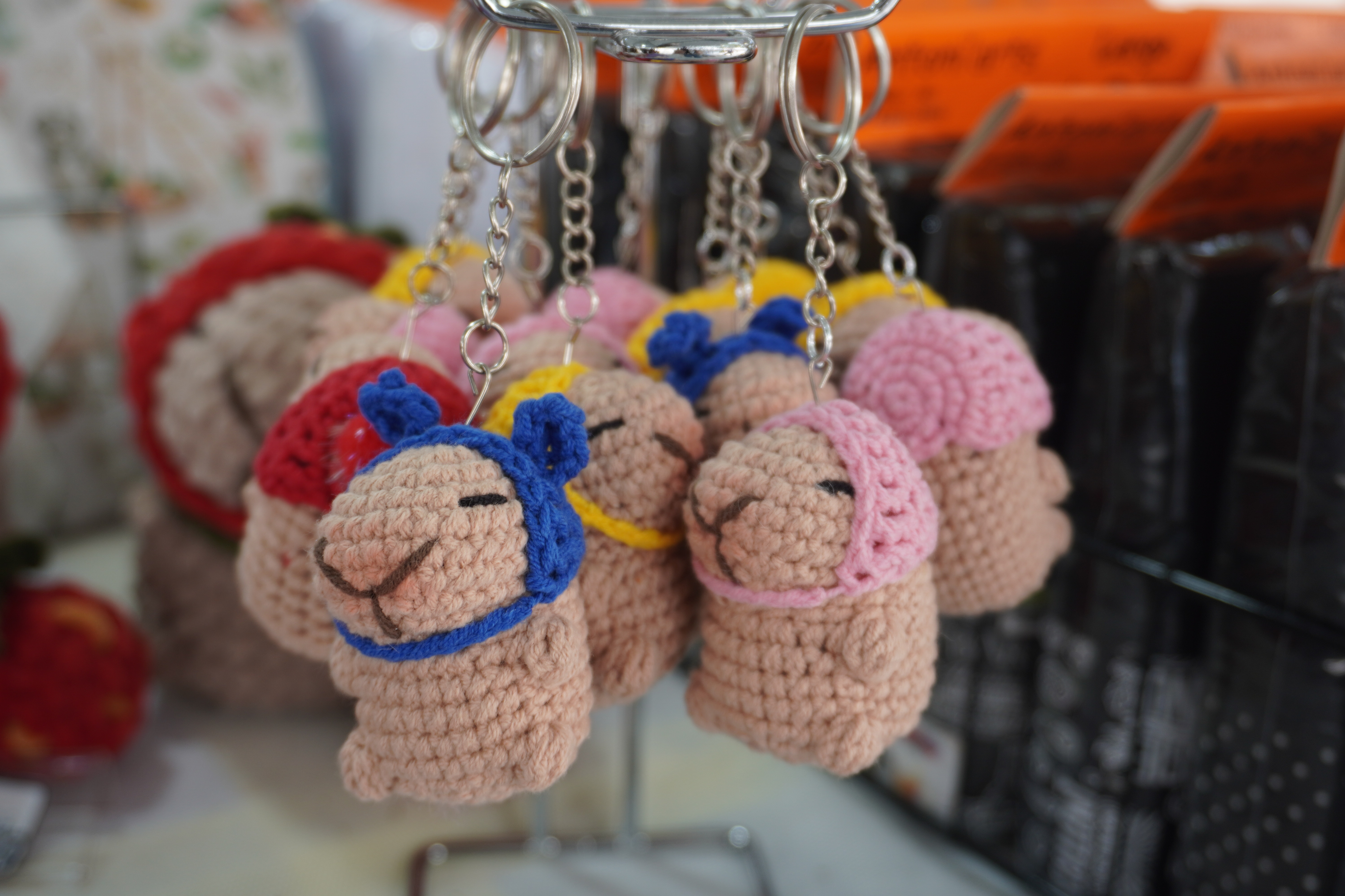 Mini capybara crochet keychains. Each cabybara wears a hat that is eithg blue, pink, red, or yellow.