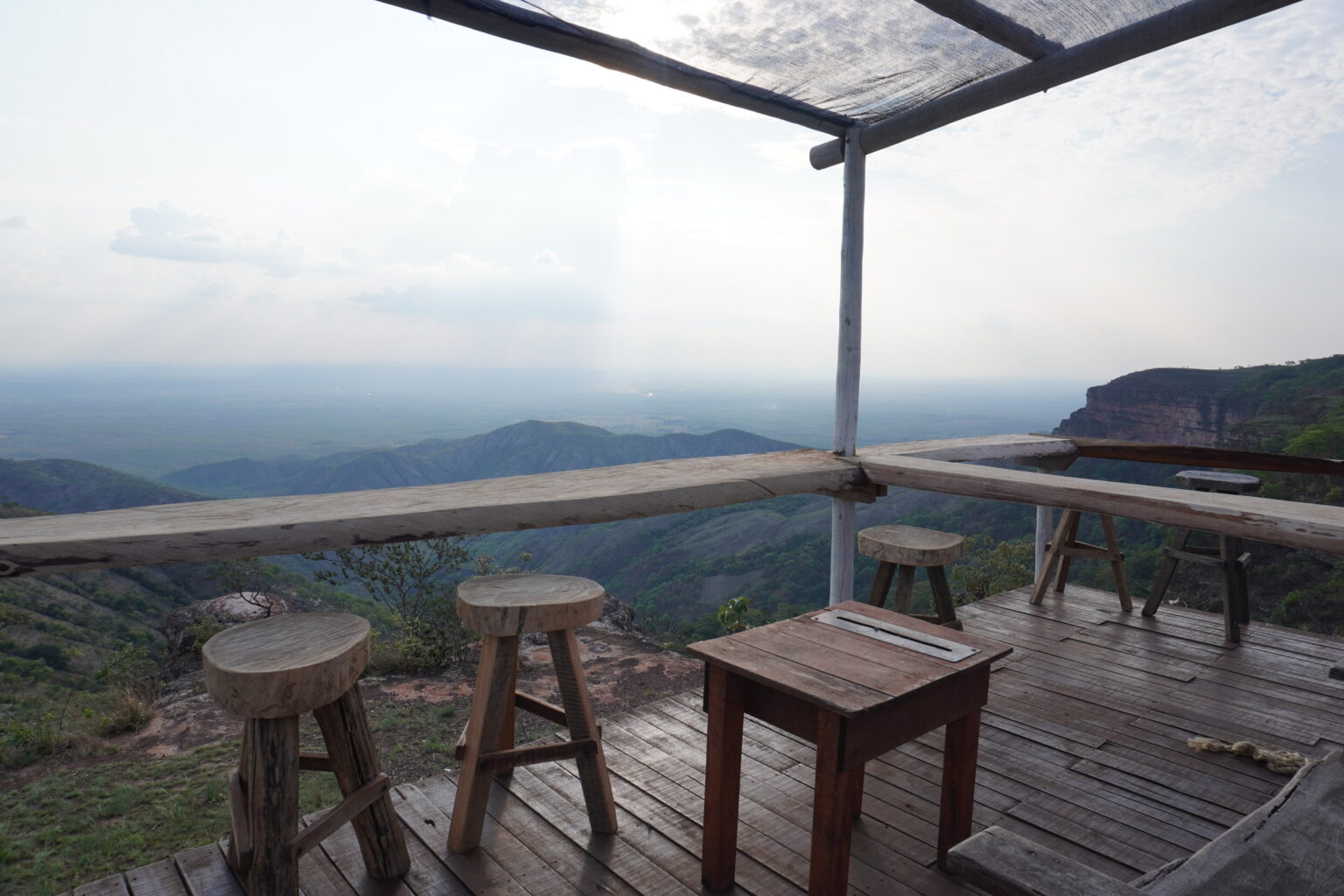 Outdoor seating at Alto do Ceu featuring a stunning view of the Chapada dos Guimaraes. Bar tables and stools are made of rustic wood.