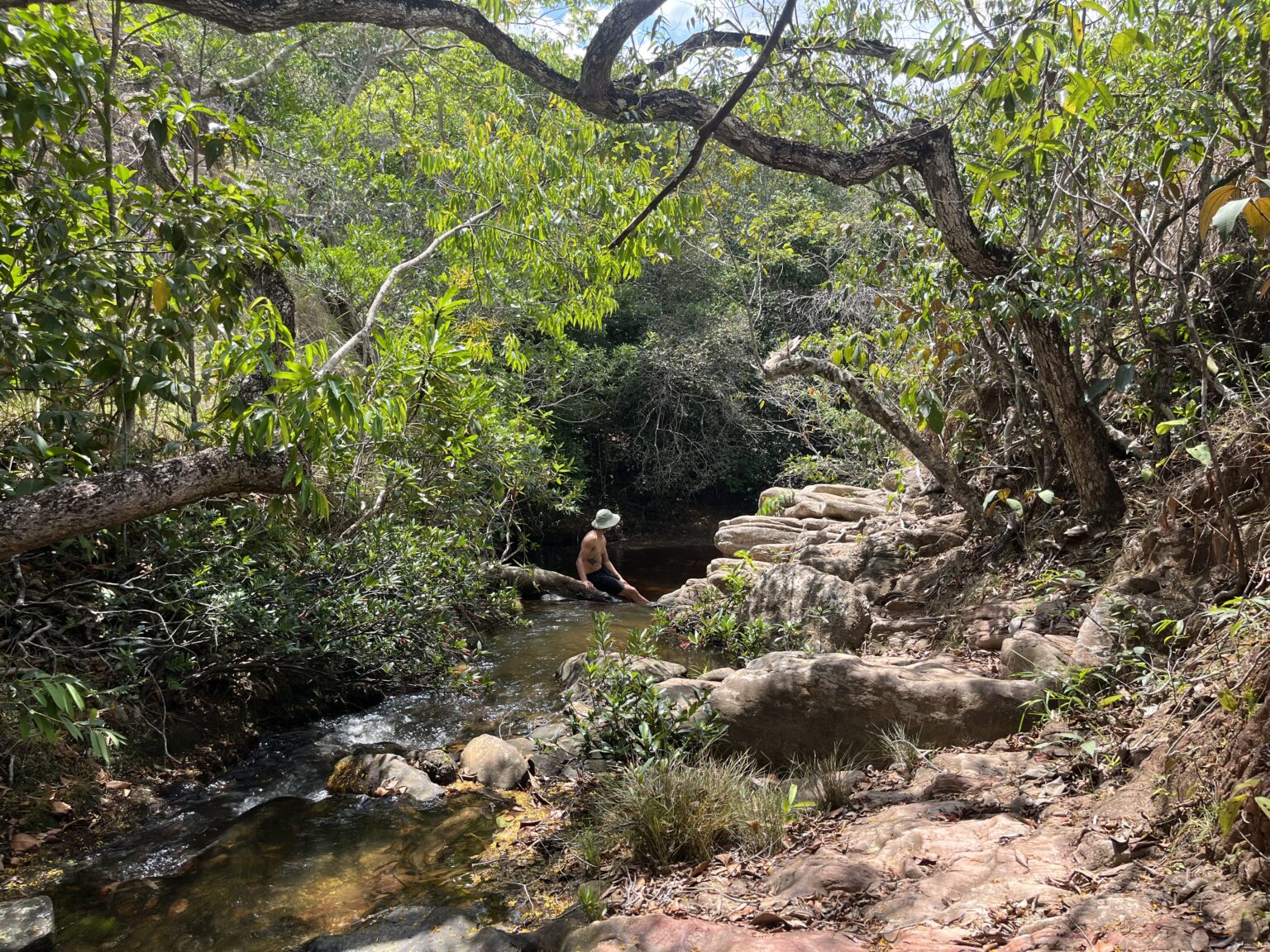 Man sitting at a small waterfall surrounded by cerrado greenery at Chapada dos Guimaraes.