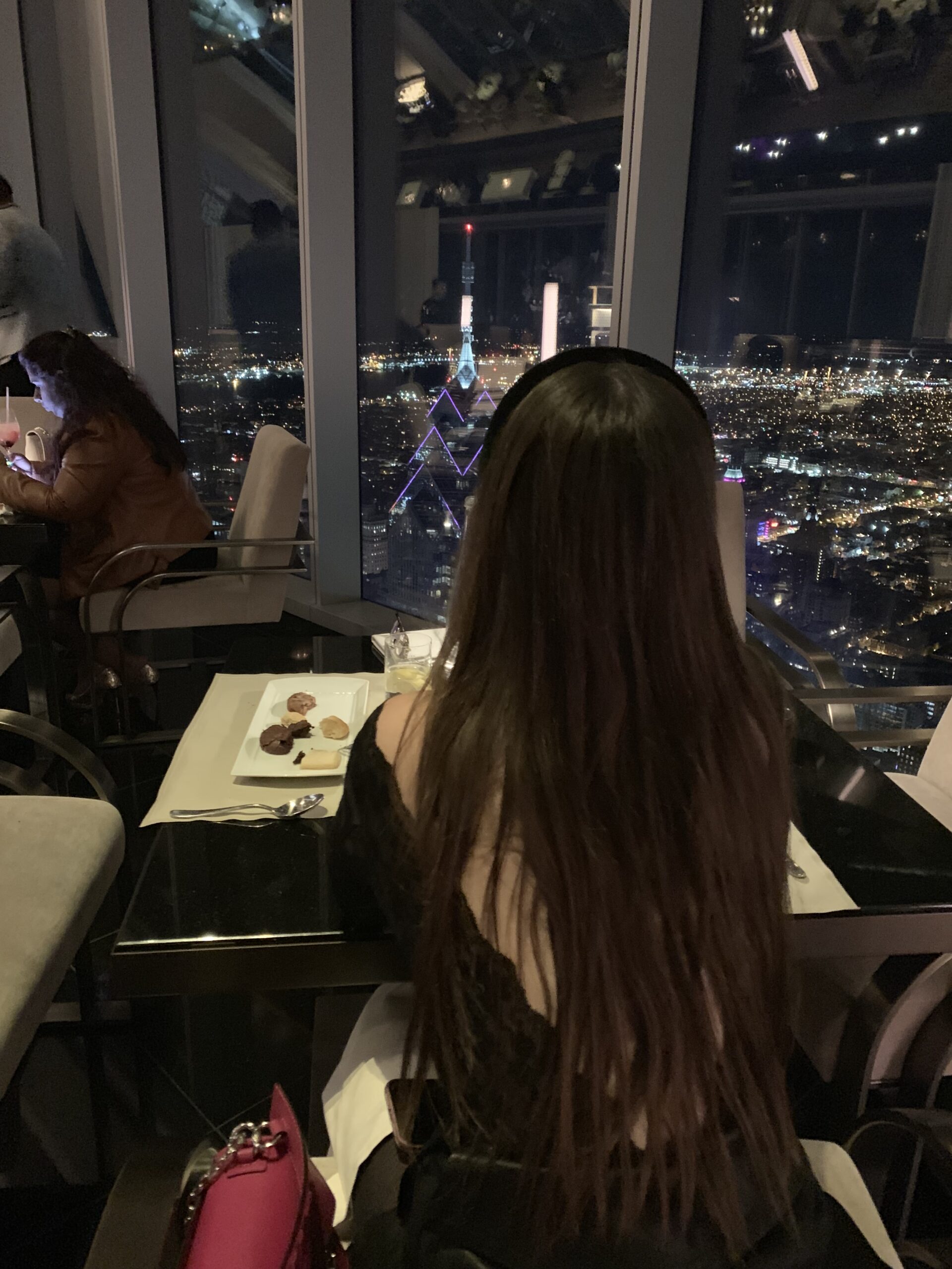 Girl sitting at JG Skyhigh in Philadelphia and contemplating a view of the city and the Liberty One building.