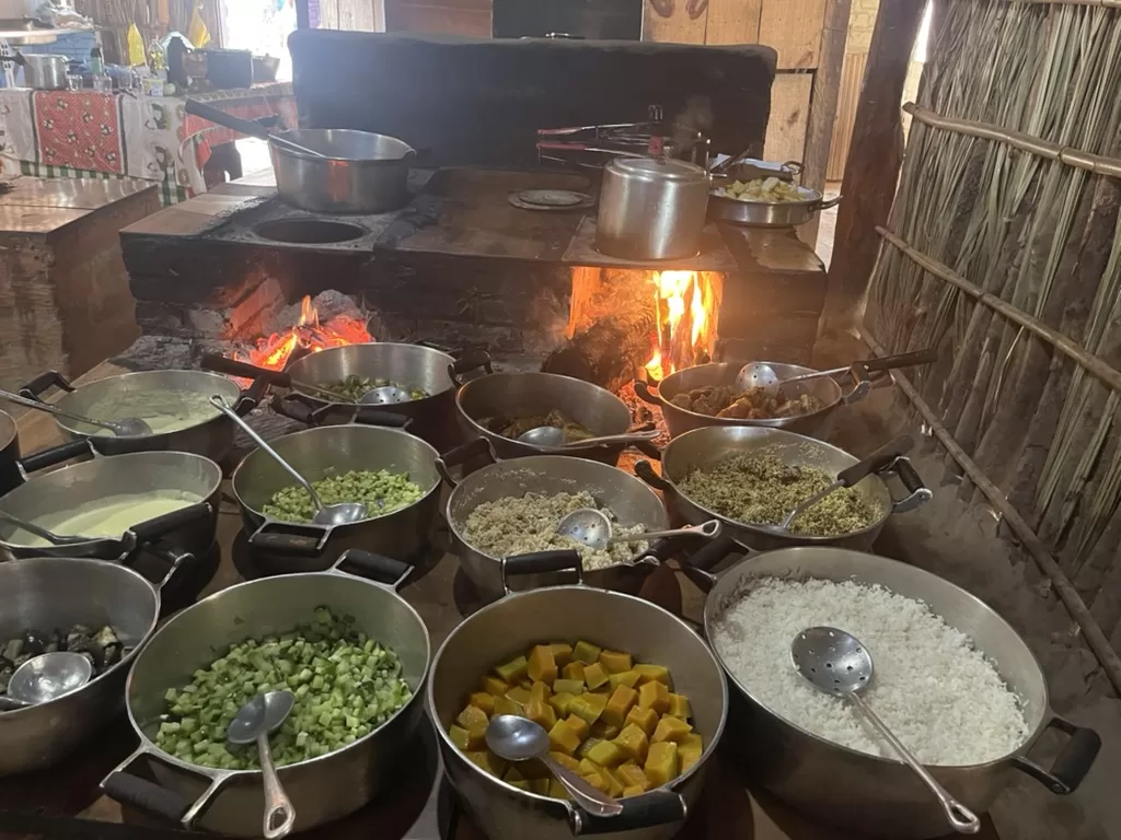 Many pans filled with food in a rural-style stove (fogão a lenha). The stove is build of bricks and fuled by burning wood.