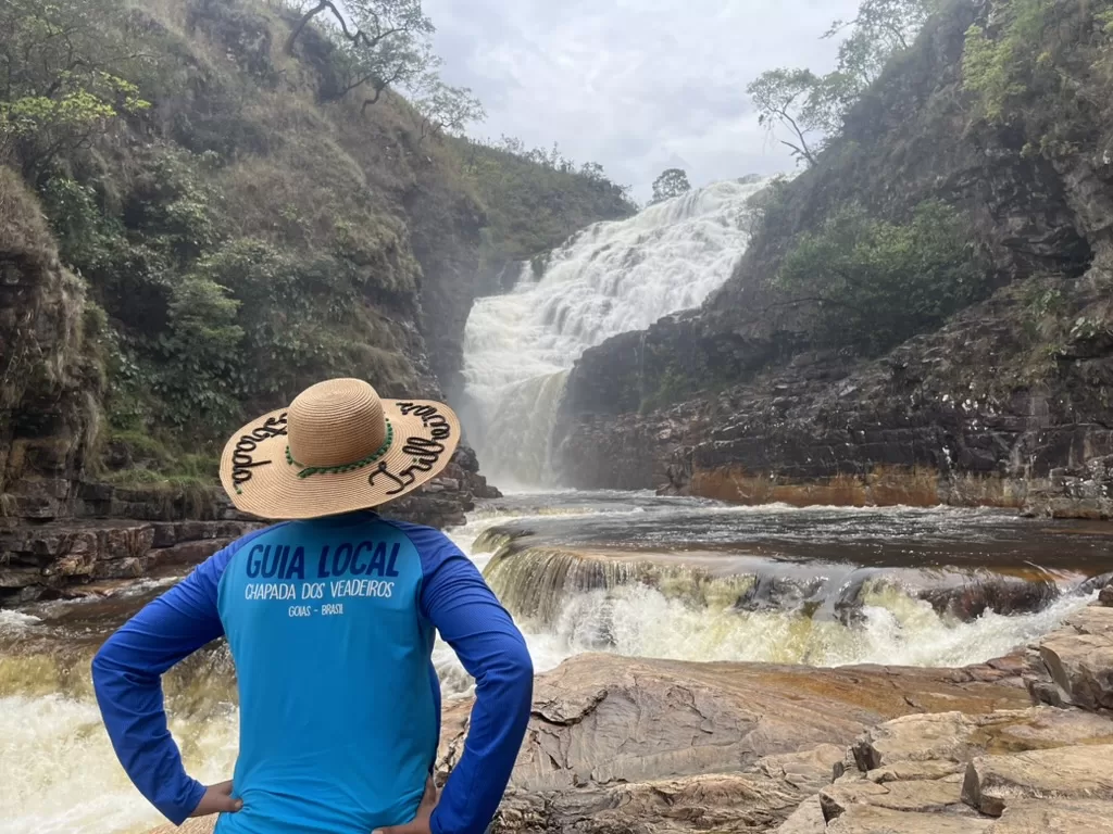 Local guide wearing a blue shirt that says "guia local chapada dos veadeiros" looking at couros falls.