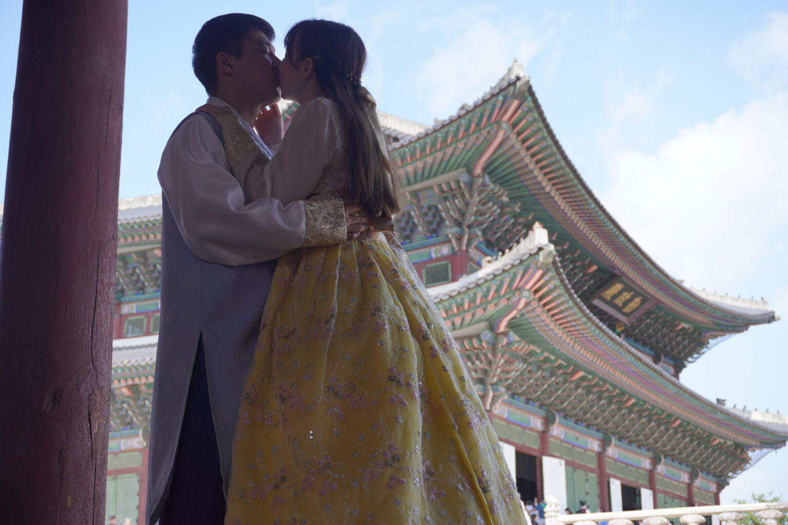 Woman and man wearing traditional Korean clothing (hanbok) and kissing in front of a palace in Seoul.