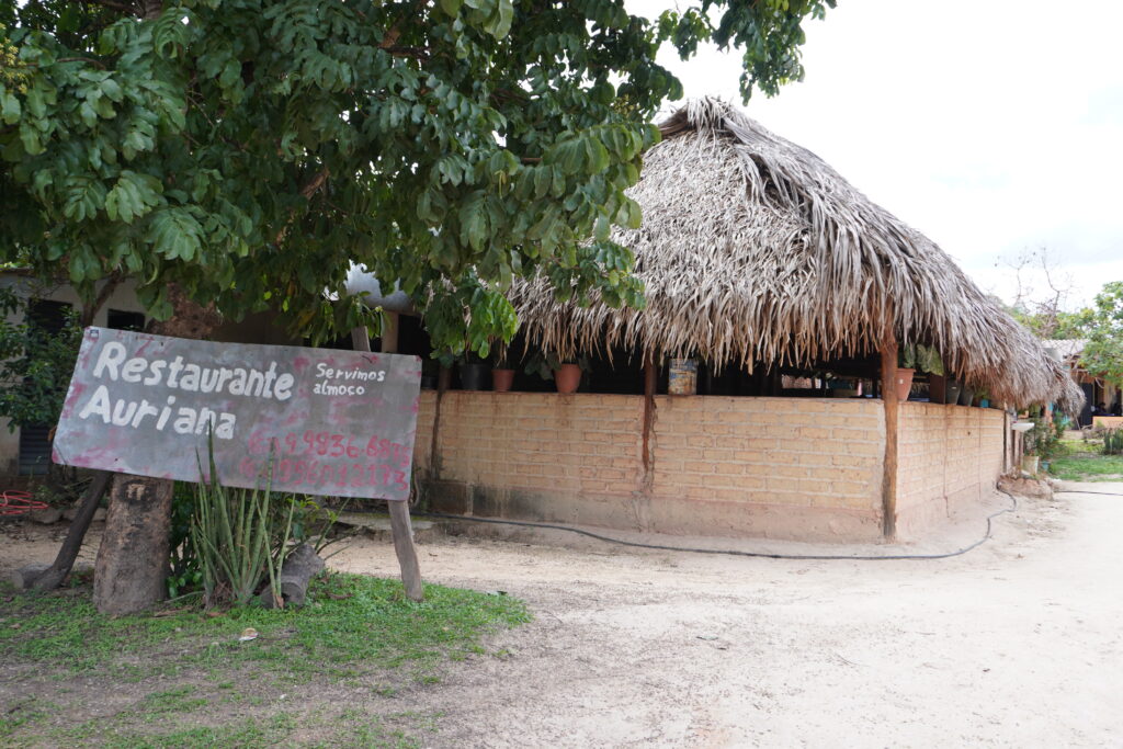 Wooden sign saying "Restaurante Auriana" in front of the brick, wood, and straw restaurant.