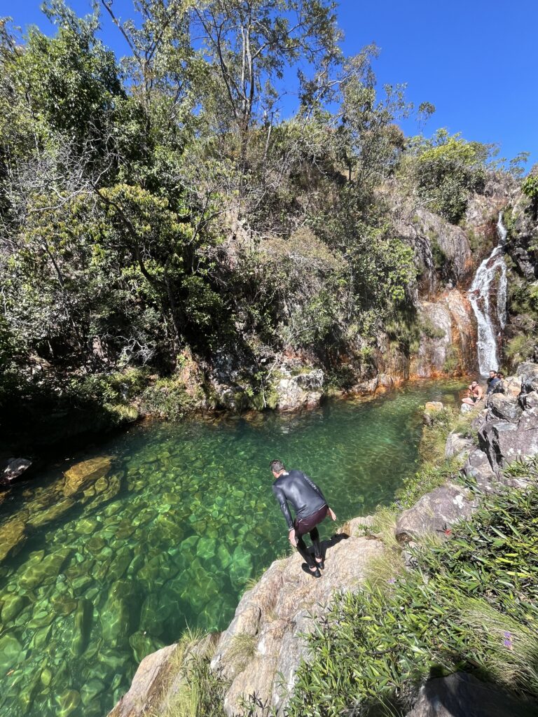 Man about to jump in a emerald-colored pool. The water is so clear that the stones at the bottom can be seen.