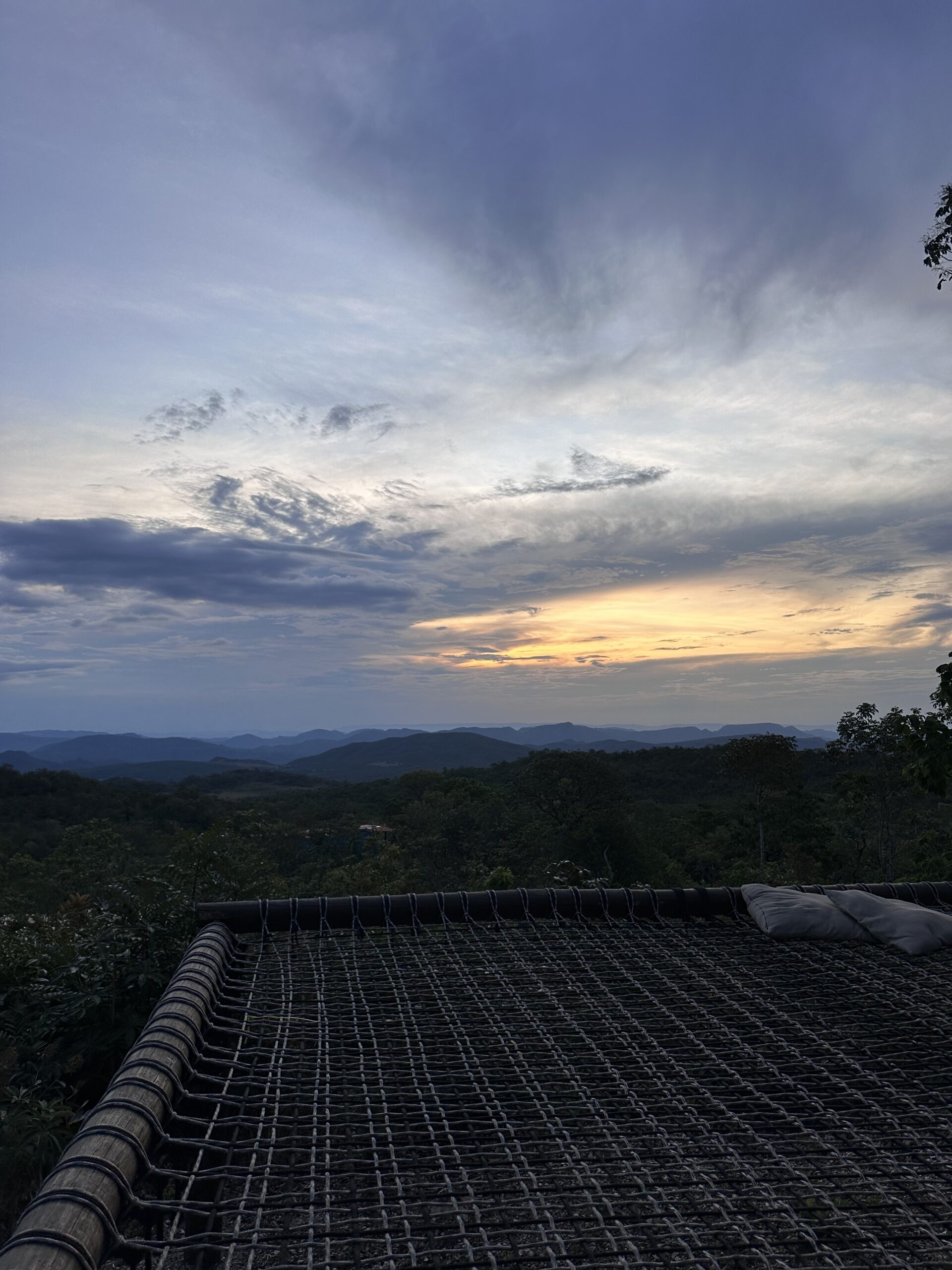 View of the sunset contrasting with mounts and the cerrado greenery. A giant net for with pillows creates an inviting atmosphere for those who want to lay down and enjoy the view.