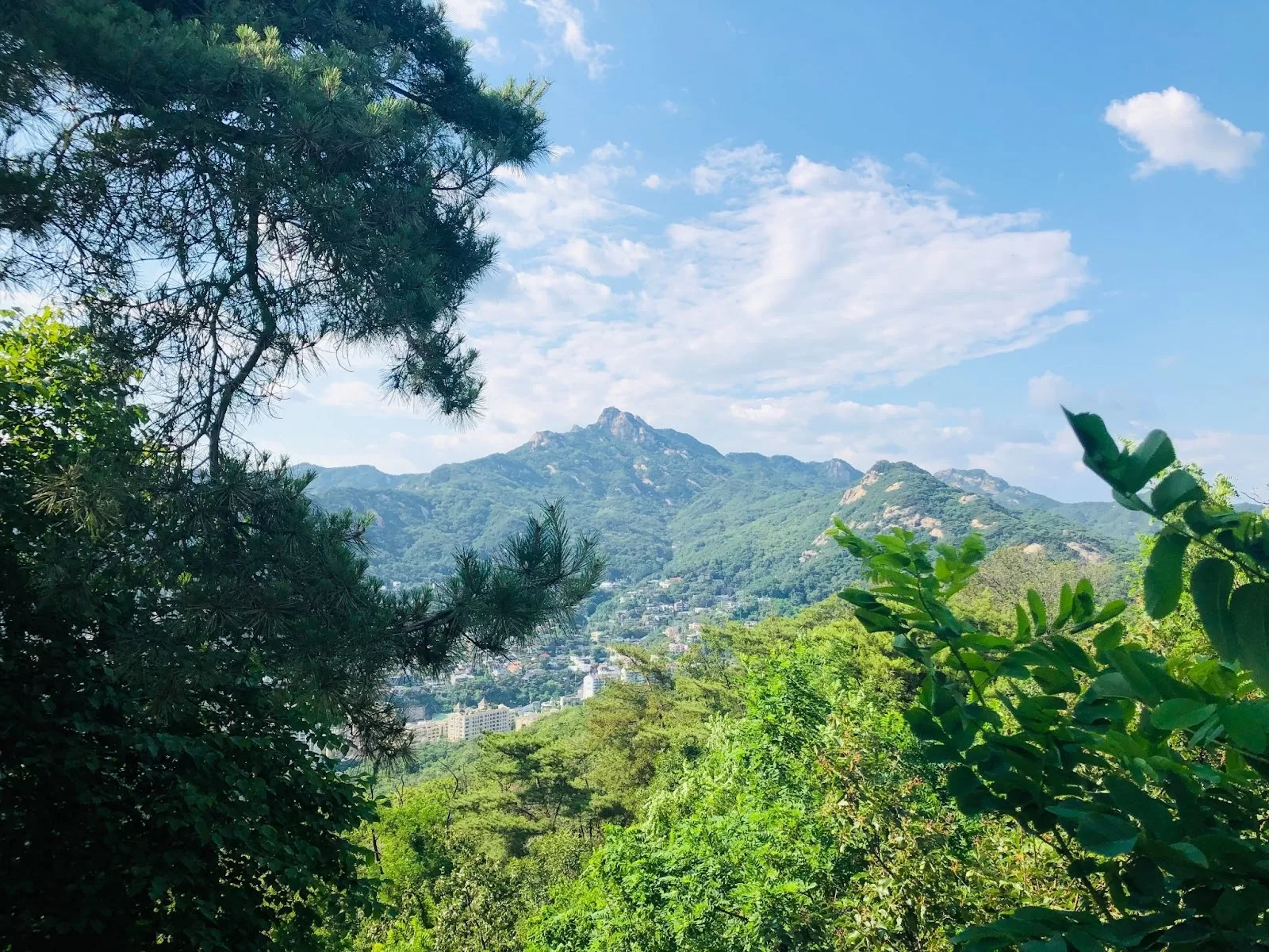 View of buildings, mountains, greenery, and blue skies.