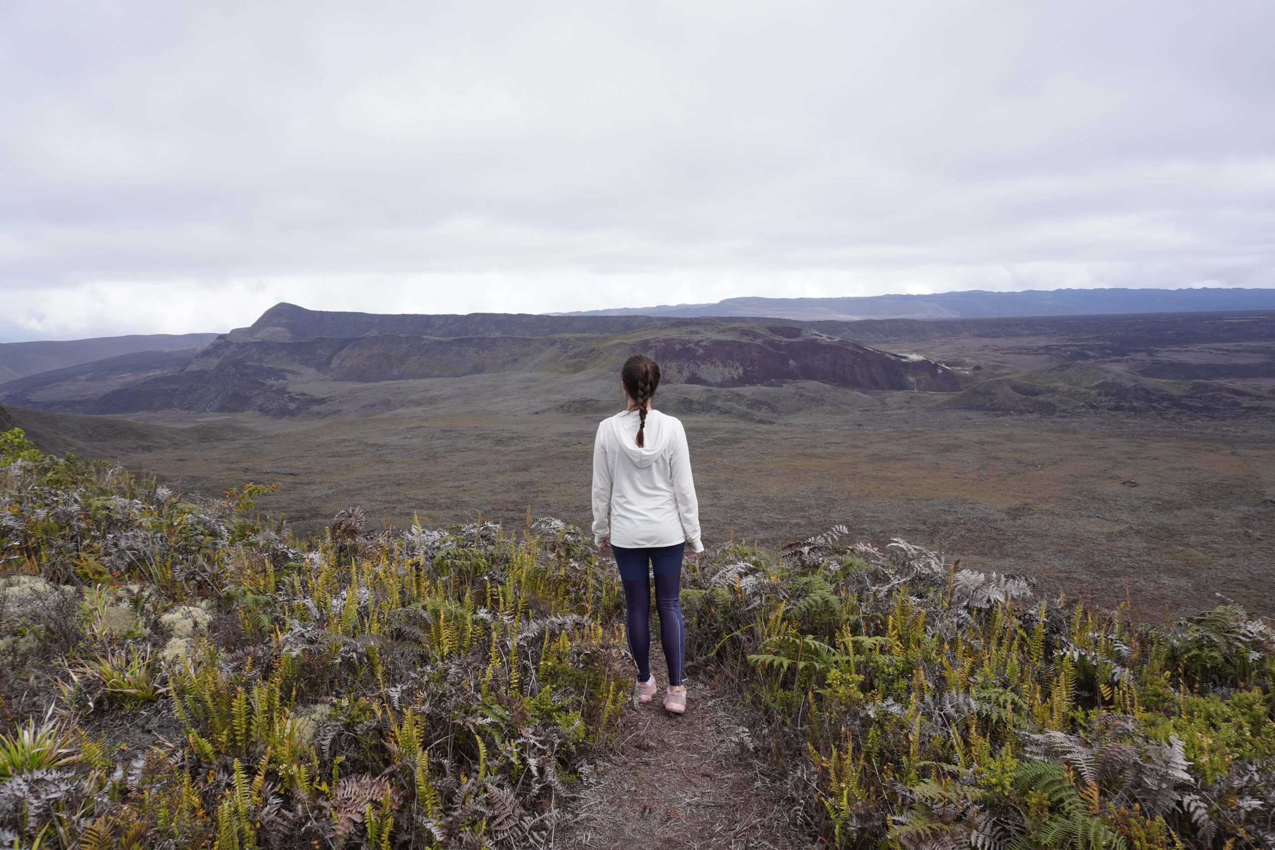 Girl standing and enjoying a view of the Volcano Sierra Negra. She is surrounded by short green vegetation.