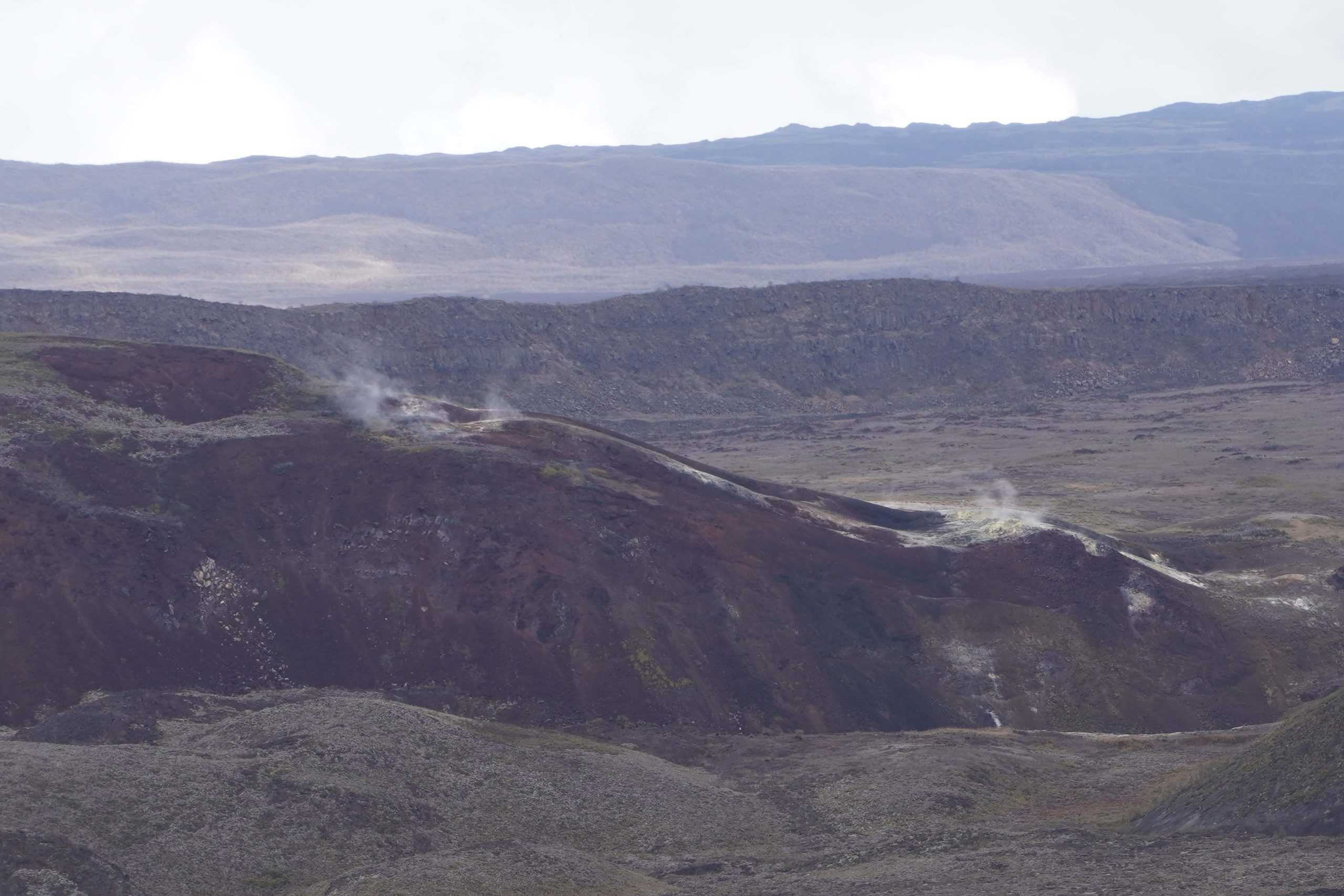 View of the sulfur mines in the crater of Volcano Sierra Negra. The mines are seen as white and smoking from a distance, which contrasts to the rest of the volcano's dark grey landscape.