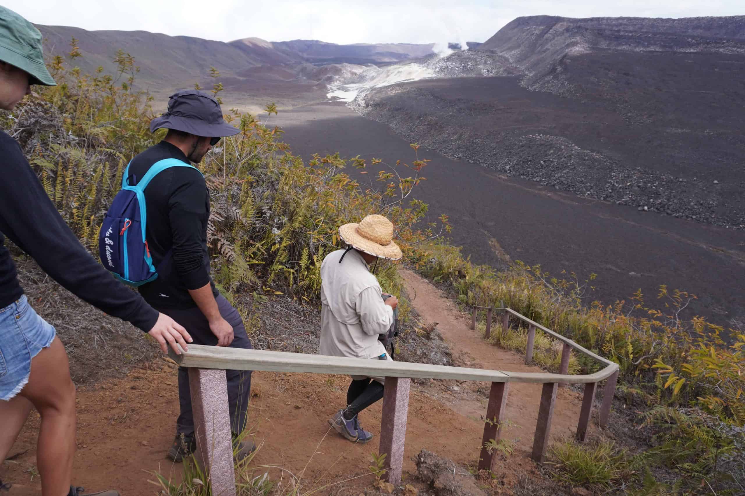 Galapagos naturalist guide guiding two dourists down a steep muddy trail in Sierra Negra with wooden handrails.