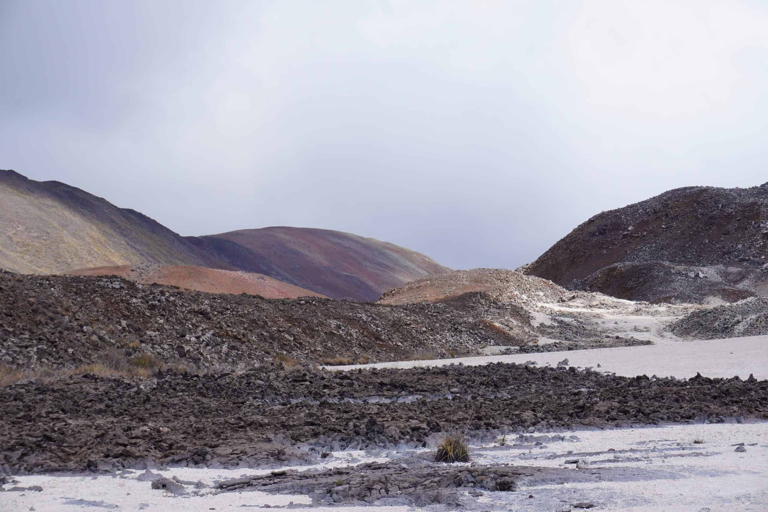 View of surrounding landscape from inside the crater of Volcano Sierra Negra. There is white areas, dark volcanic rock areas, and a colorful mountain.