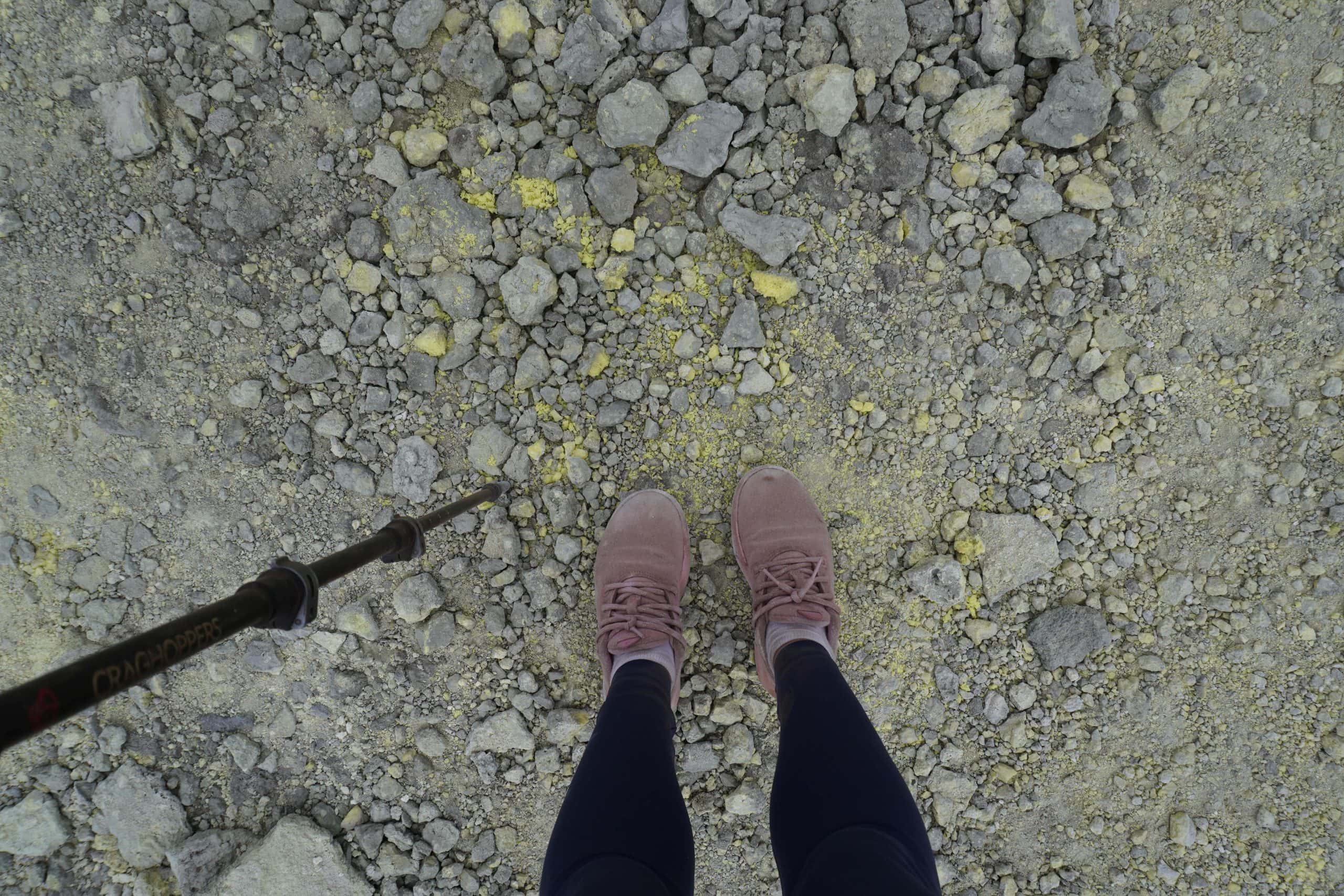 Girl standing with a hiking stick on top of gravel and sulfur during the Sierra Negra Volcano Hike.