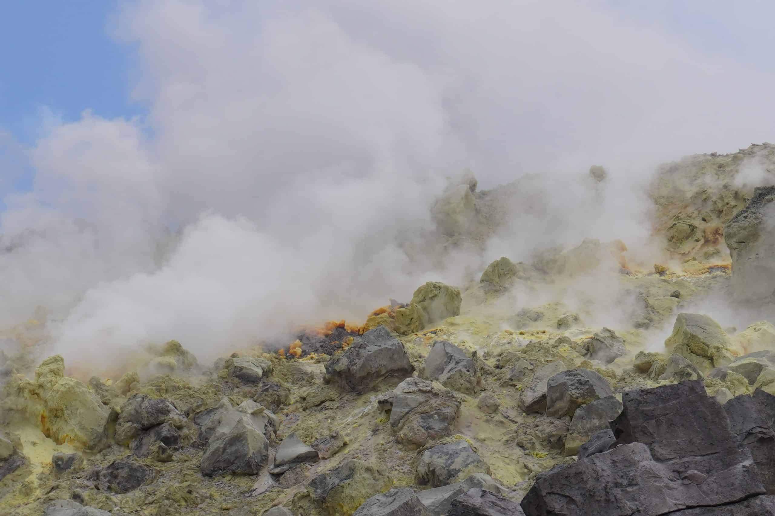Actively smoking sulfur mines in the Sierra Negra Volcano. The sulfur is yellow and the clouds coming out of it are white.