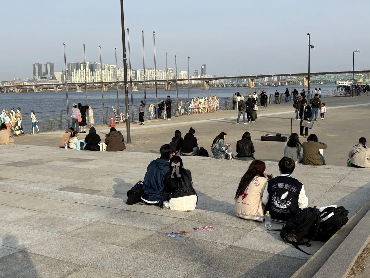 Lots of people sitting by and walking along the Han river in a clear-sky afternoon.