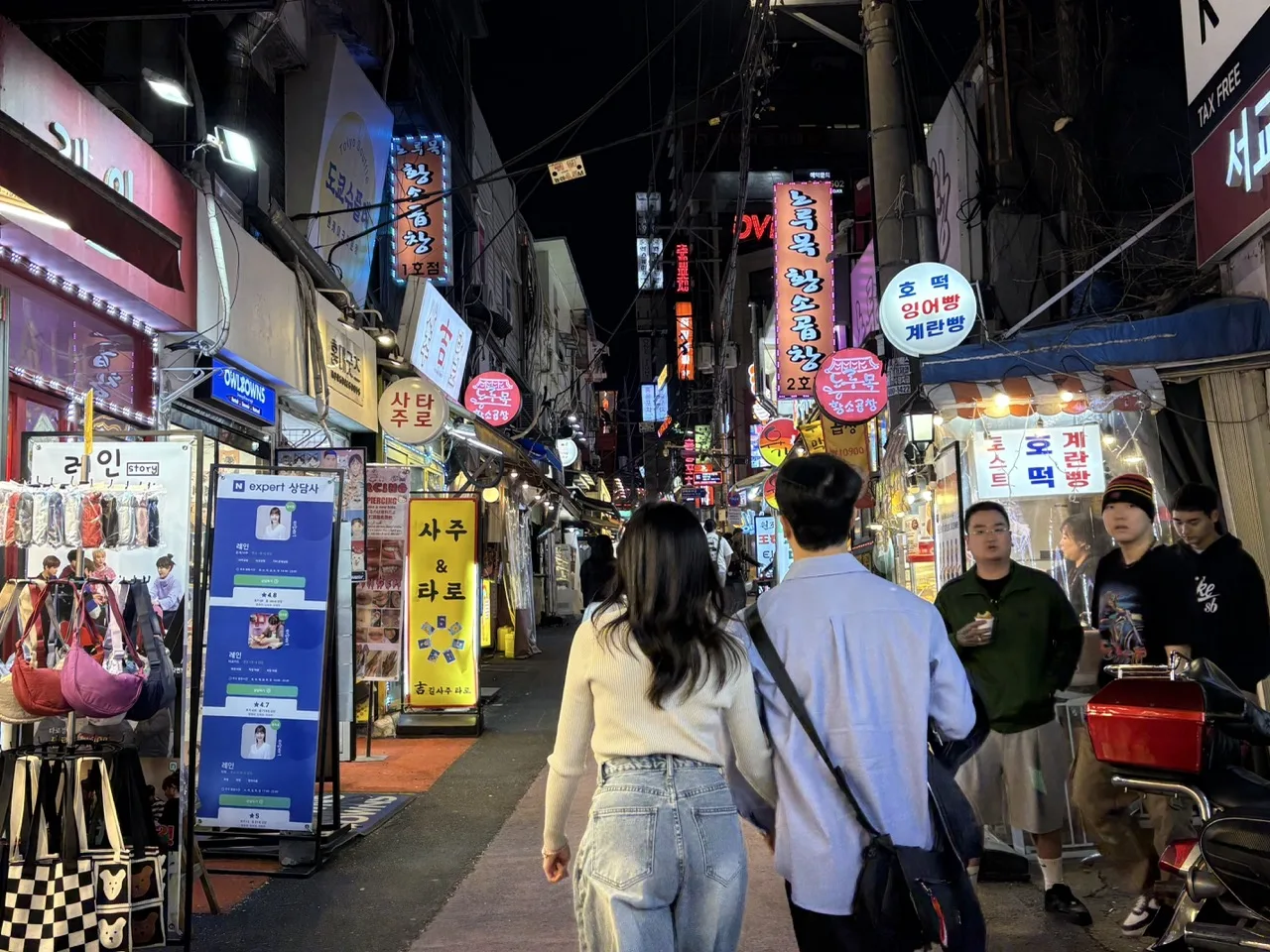 Couple waking in the Hongdae neighborhood at night, surrounded by many shops with neon signs