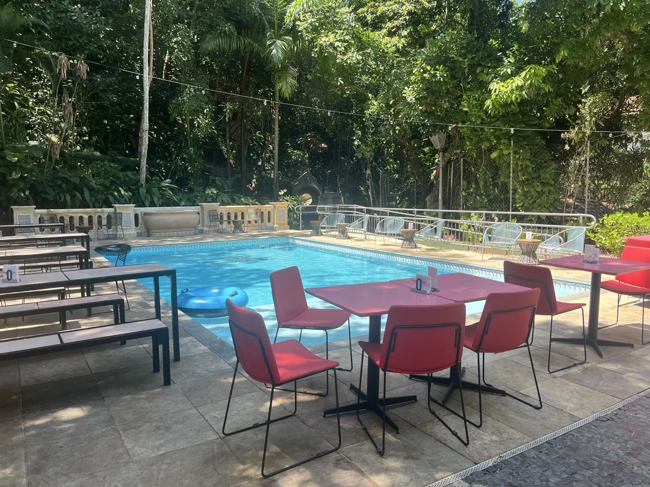 Pool area of Jo&Joe hostel in Rio, surrounded by nature and with restaurant tables.