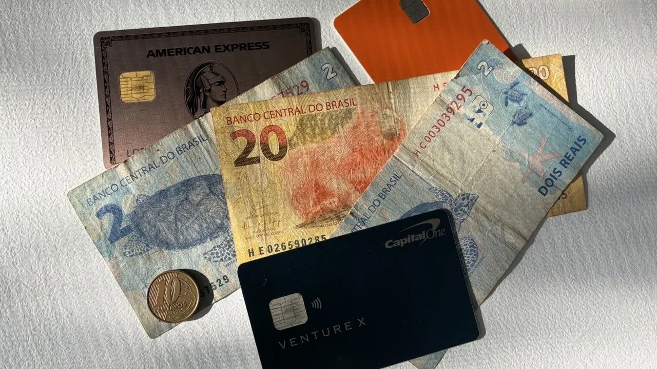 Bills of Brazilial real cash piled with international credit cards such as the Capital One Venture X and the American Express Gold